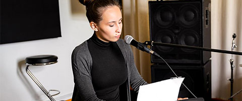 Woman singing and playing keyboard in a studio
