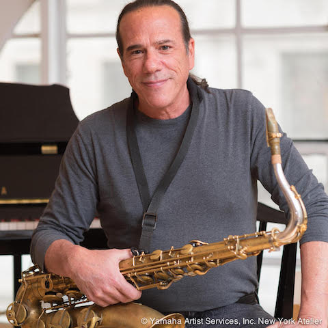 Dan Moretti sitting in front of a piano with his saxophone in hand