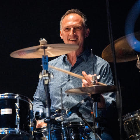Mark Walker playing drums in a blue collared shirt
