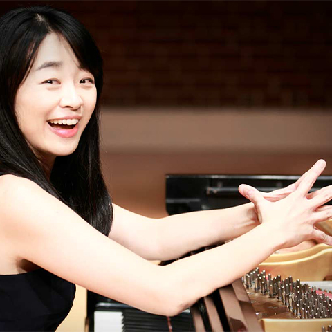 a woman sitting, smiling, at a grand piano