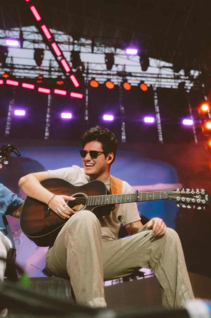 a man sitting on the edge of a stage playing an acoustic guitar