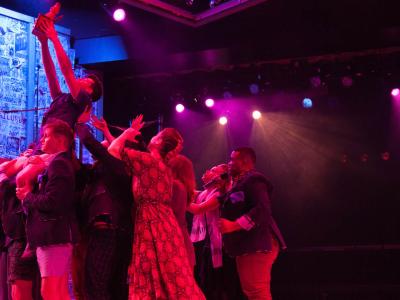 Performers on a colorfully lit stage acting out a dramatic scene