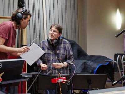 Two musicians in a recording studio leaning in and talking