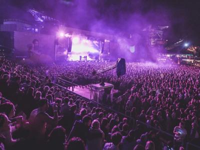 Huge crowd at an outdoor music festival with dramatic lights and smoke effects