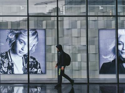Young person in street wear walking past large portraits in a glass building