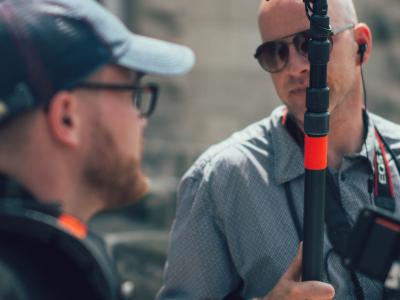 Two men holding recording equipment looking at each other