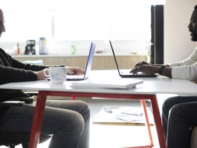 Two men sitting across the table with their laptops open