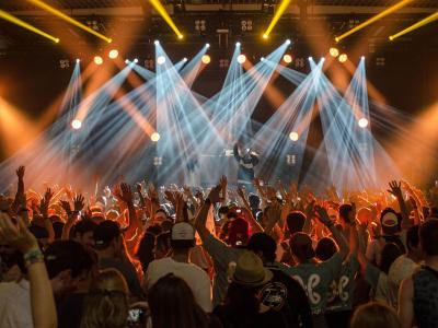 Large crowd dancing in front of a stage with laser light effects