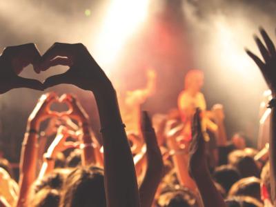 People in a crowd making heart hands at a musician on stage