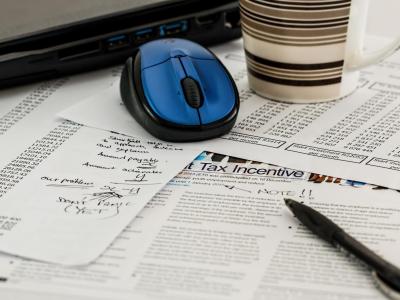 Spreadsheets and tax documents on a table with a computer mouse and coffee mug