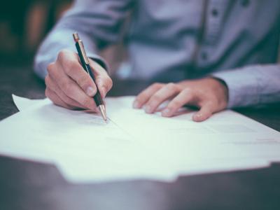 Person in business attire writing on sheets of paper with a pen