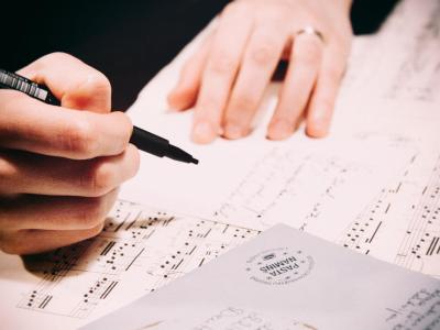 Person holding a pen adding annotations to sheet music