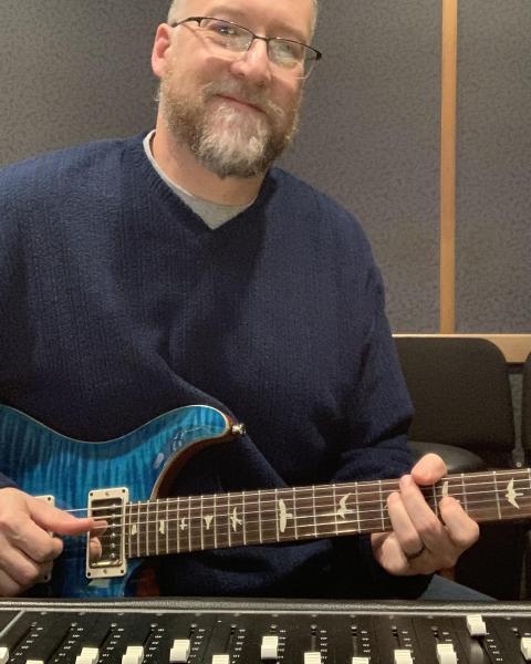 Frankie Price holding a guitar while smiling