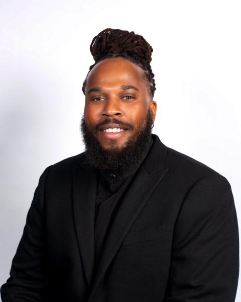 Bassist Christoff Glaude poses in an all-black suit.