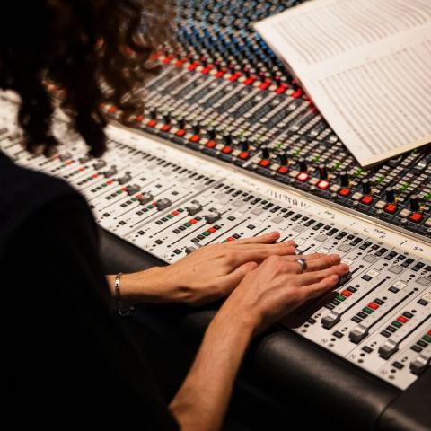 Producer adjusting levels on a soundboard and looking at sheet music