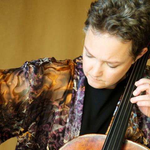 Rhonda Rider looking down playing the cello with a tan background