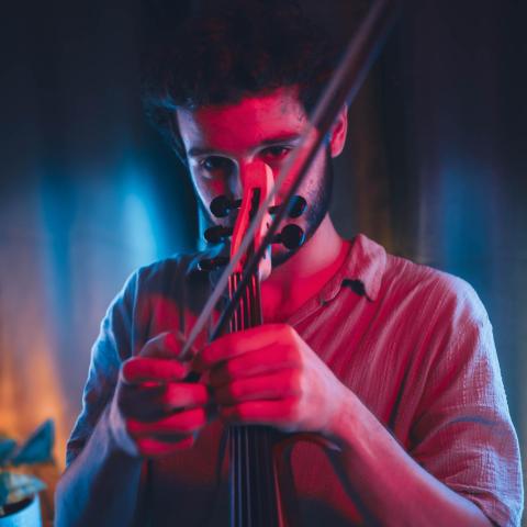 Omer Kochba playing a violin under dramatic red and blue lighting, focused intently on the instrument.