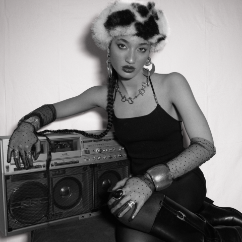Black-and-white portrait of Jazz Cuti in a fur hat, gloves, and boots posing with a vintage boombox, styled with bold jewelry and a confident expression.