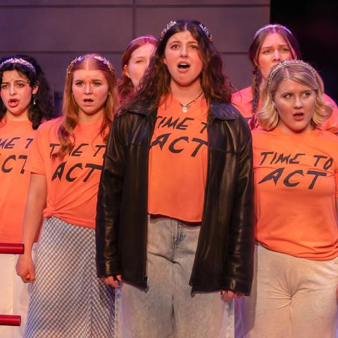 Performers in 'Time to Act' singing together in orange shirts