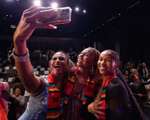 Photo of three smiling Black women, posing with their kente cloths at the Jabulani celebration.