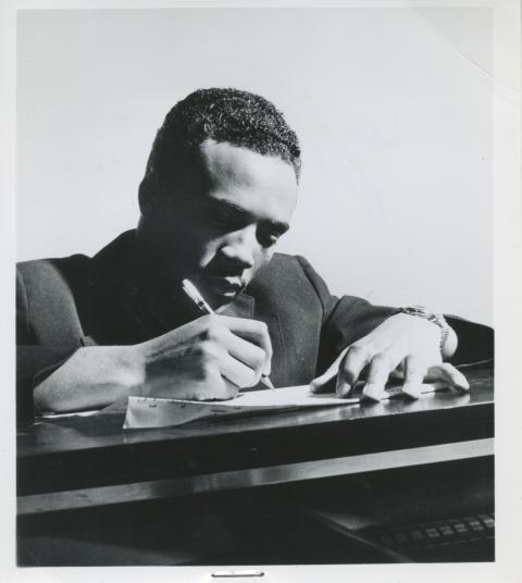 A young Quincy Jones sitting at a desk and handwriting a musical composition