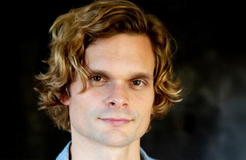 Andrew Durand headshot: grinning in front of a black backdrop.