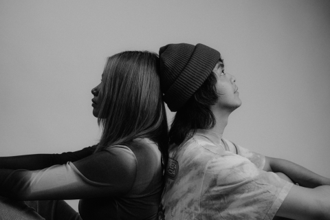 girl and boy sitting back to back with hands on knees looking forward. black and white filtered image