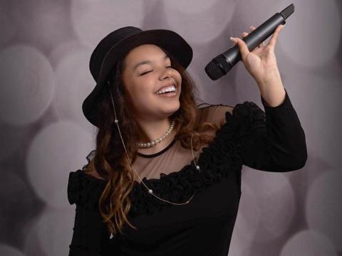 Formal portrait of Paris Pineyro with her eyes closed and holding a microphone above her head