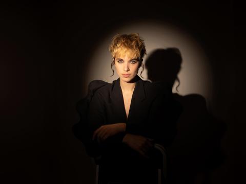 The artist beccs posing against a dark background with a spotlight on her