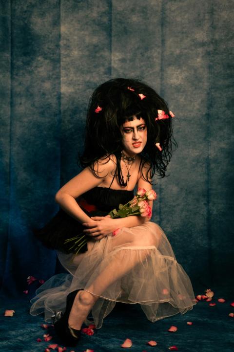 Leila Lamb posing with flower pedals around her against a stylized gray backdrop