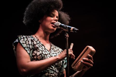 Melvis Santa sings at a microphone and plays claves