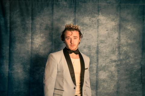 Pat Kennedy wearing a crown and posing against a gray backdrop