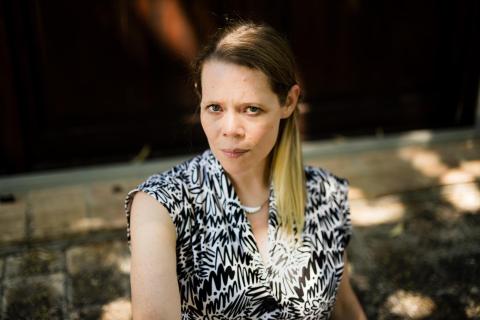 Caroline Davis looks directly at the camera. They have straight blond hair pulled in a side ponytail and a black and white patterned shirt