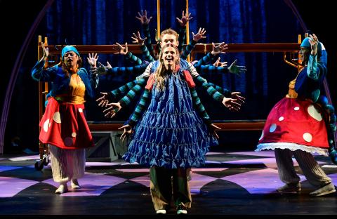 Theater students performing on stage in 'Alice by Heart' in a row with their arms spread out making a circle of arms