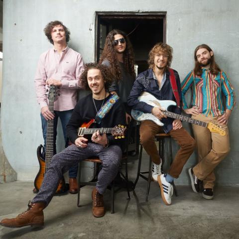 The band Dogs in a Pile pose together holding their instruments and smiling