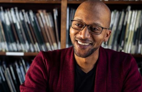 Headshot of Kevin Haden in a red suit with a black shirt in front of book shelves
