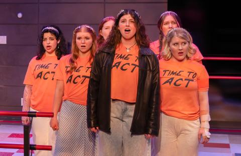 Performers in 'Time to Act' singing together in orange shirts