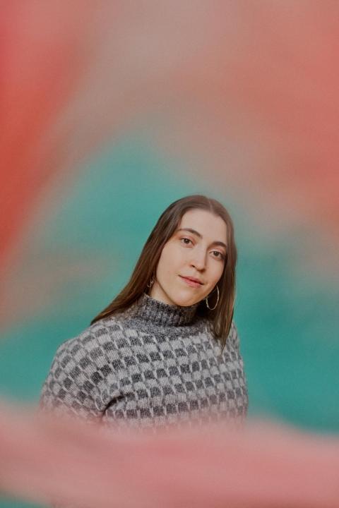 Alisa Amador looks at the camera, she has straight brown hair, gold hoop earrings, and a patterned gray sweater