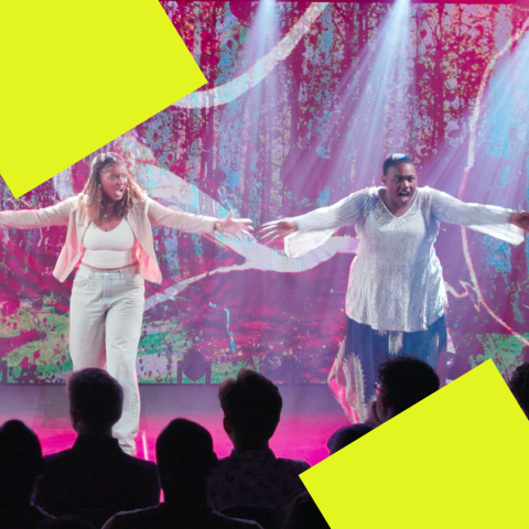 Two actors sing on stage with their arms outstretched.