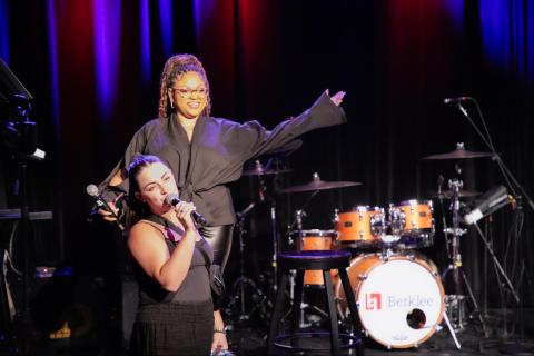 Woman on stage holding a guitar with drums on the right