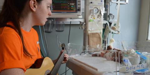 Young woman playing guitar to a newborn baby in the hospital